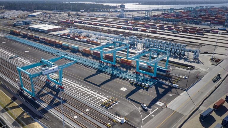 Aerial view of the central rail yard at Norfolk International Terminals, Port of Virginia. The image shows a network of rail tracks, rail mounted gantry cranes and containers in front of the terminal's container stacks.